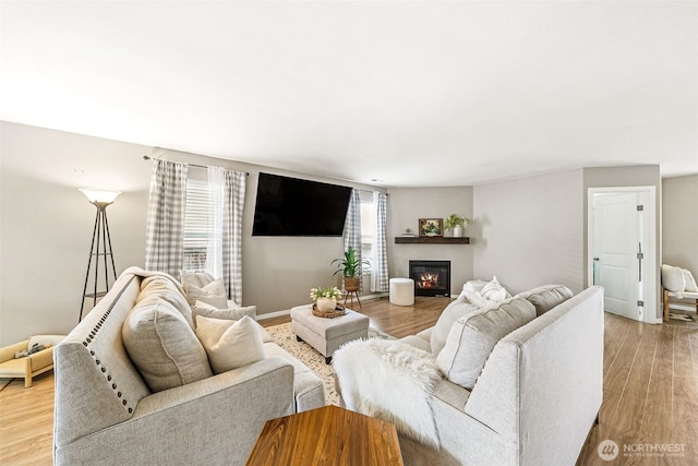 living area featuring a glass covered fireplace, light wood-type flooring, and baseboards