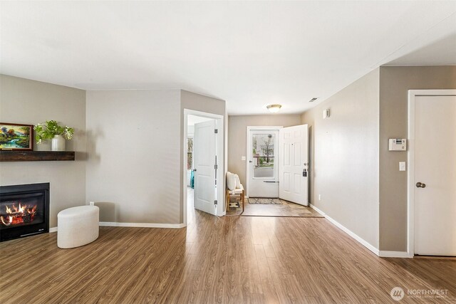 foyer featuring a glass covered fireplace, wood finished floors, and baseboards