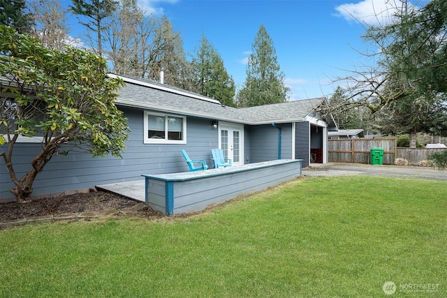 rear view of property featuring fence, driveway, french doors, a lawn, and roof mounted solar panels