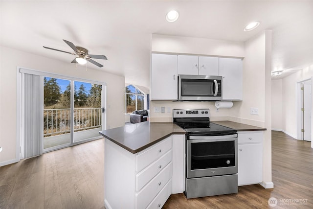 kitchen with stainless steel appliances, dark countertops, a peninsula, and dark wood finished floors