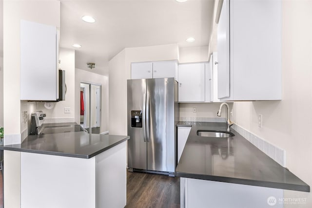 kitchen featuring stainless steel appliances, dark countertops, white cabinetry, a sink, and a peninsula