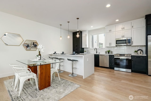 kitchen featuring backsplash, appliances with stainless steel finishes, light wood-style floors, a peninsula, and a kitchen bar