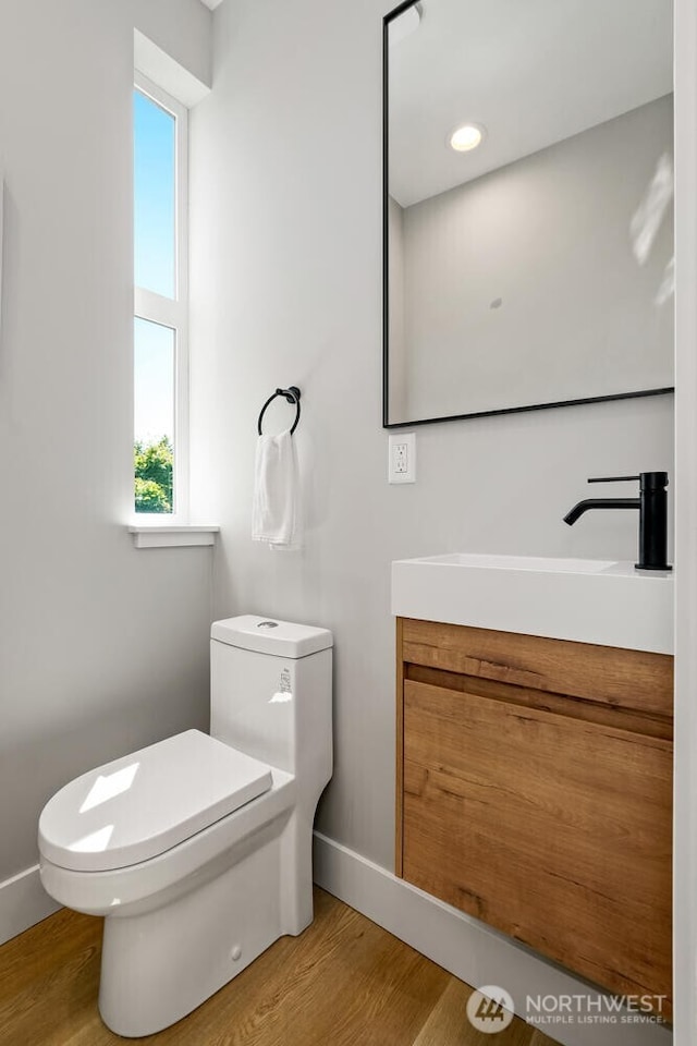 half bath featuring baseboards, vanity, toilet, and wood finished floors