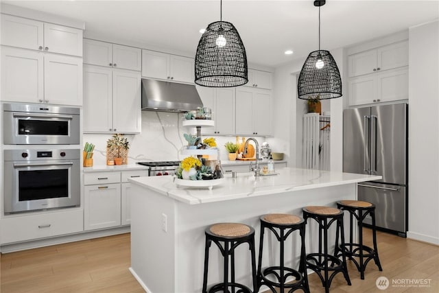 kitchen featuring a breakfast bar, appliances with stainless steel finishes, a sink, light wood-type flooring, and under cabinet range hood