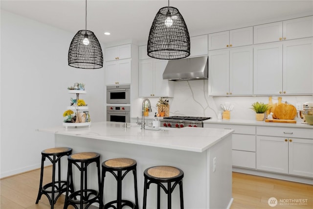 kitchen featuring light wood-style flooring, a breakfast bar, range hood, stainless steel appliances, and white cabinetry