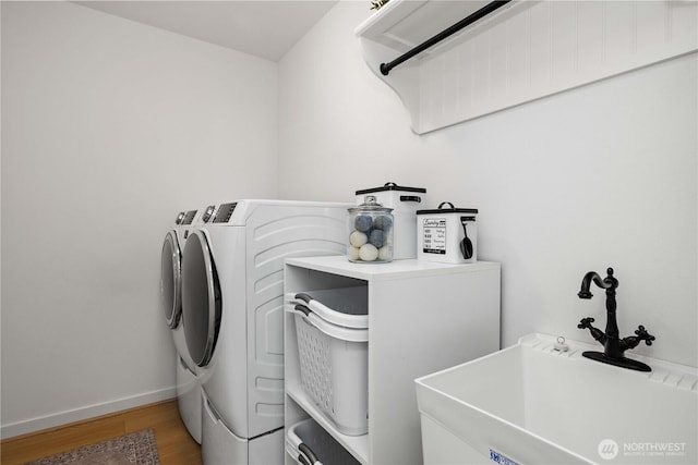 washroom featuring washing machine and clothes dryer, a sink, wood finished floors, laundry area, and baseboards