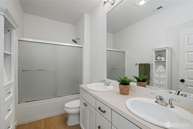 bathroom with shower / bath combination with glass door, visible vents, a sink, and wood finished floors