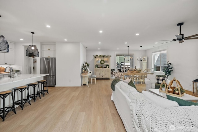 living room featuring ceiling fan with notable chandelier, baseboards, light wood-style flooring, and recessed lighting