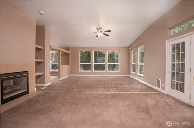 unfurnished living room featuring a wealth of natural light, built in features, carpet flooring, and a tiled fireplace