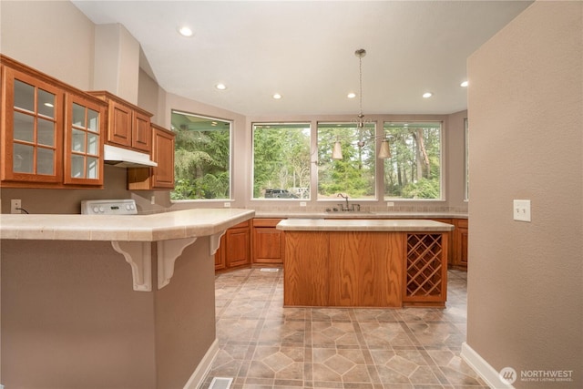 kitchen with under cabinet range hood, a sink, recessed lighting, a breakfast bar area, and glass insert cabinets