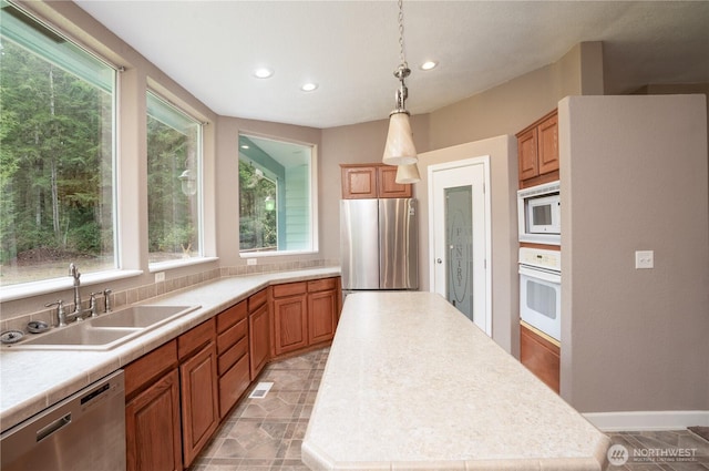 kitchen with pendant lighting, a sink, a kitchen island, stainless steel appliances, and light countertops