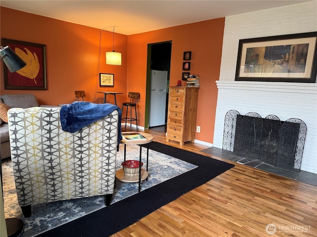 living area with a brick fireplace, baseboards, and wood finished floors