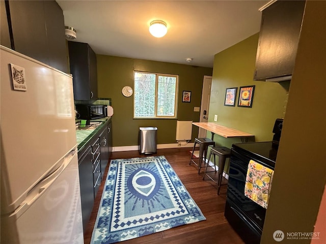 kitchen with dark wood-style floors, light countertops, black appliances, dark cabinetry, and baseboards