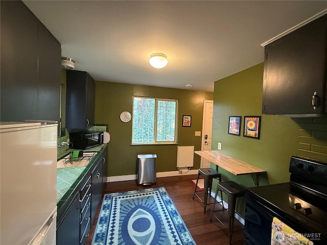 kitchen featuring tile countertops, black appliances, baseboards, and dark wood-style floors