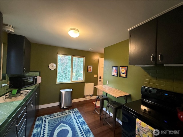 kitchen featuring tile countertops, dark wood-style flooring, a sink, baseboards, and black appliances