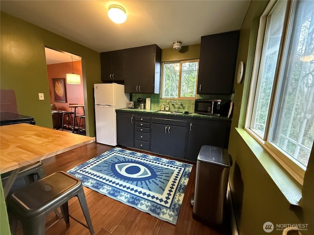 kitchen with dark wood-type flooring, freestanding refrigerator, a sink, and tasteful backsplash