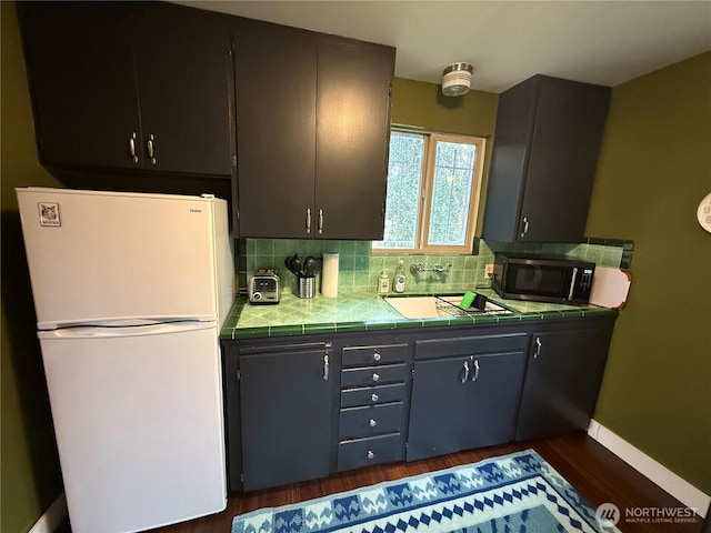 kitchen featuring decorative backsplash, tile counters, freestanding refrigerator, stainless steel microwave, and mail area