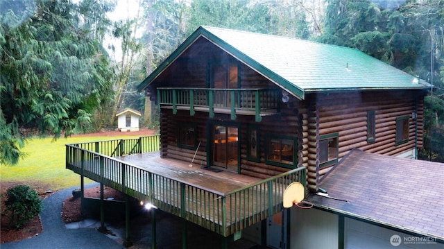 rear view of property featuring a deck, a lawn, log siding, and a balcony