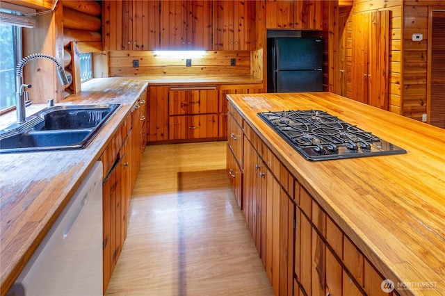 kitchen with a sink, light wood-style floors, wooden counters, log walls, and black appliances