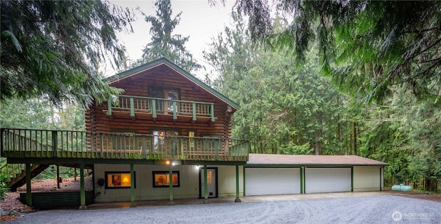 cabin featuring an attached garage, a balcony, log siding, driveway, and stairs