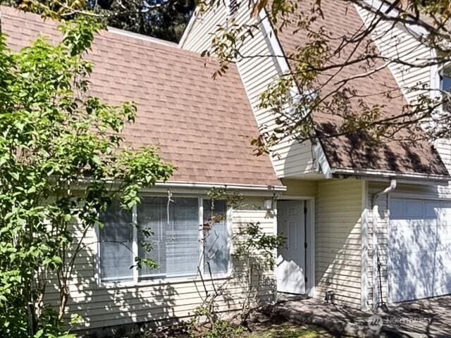 exterior space featuring a shingled roof and an attached garage