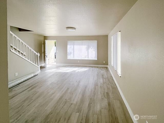 unfurnished living room with stairs, a textured ceiling, wood finished floors, and baseboards