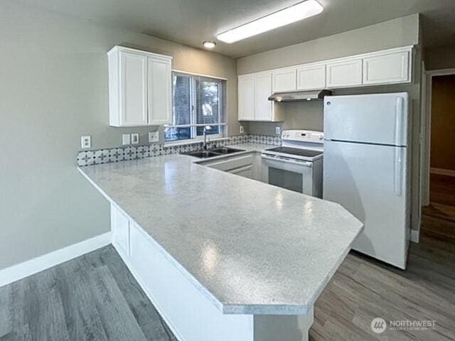 kitchen featuring white appliances, a peninsula, light countertops, under cabinet range hood, and a sink