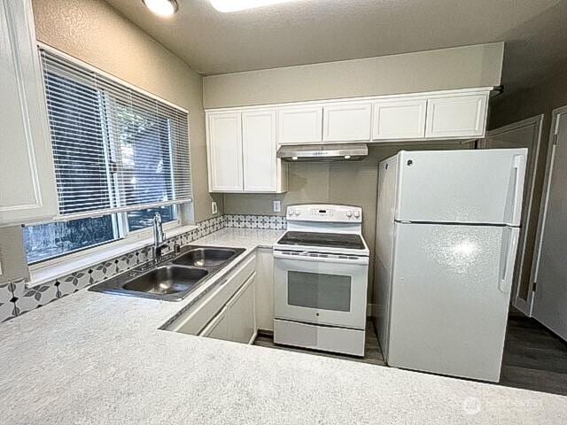 kitchen with white appliances, white cabinetry, a sink, and under cabinet range hood