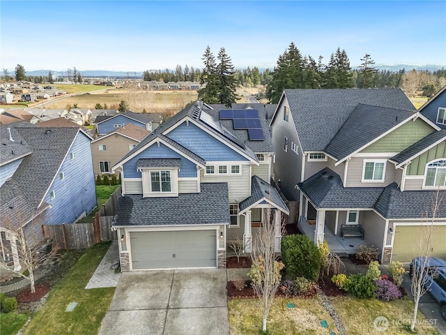 view of front facade with fence, a residential view, roof mounted solar panels, stone siding, and driveway