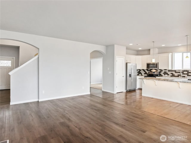 unfurnished living room featuring dark wood finished floors, recessed lighting, arched walkways, and baseboards