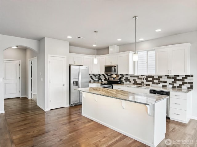 kitchen featuring arched walkways, a sink, stainless steel appliances, white cabinetry, and a center island