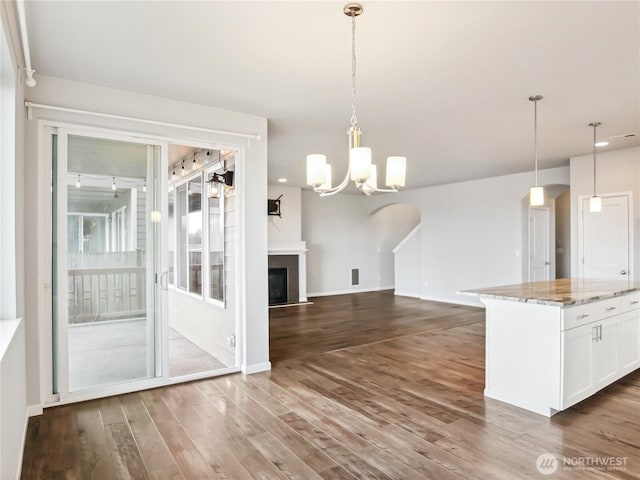 kitchen with light stone countertops, dark wood finished floors, hanging light fixtures, white cabinets, and a chandelier