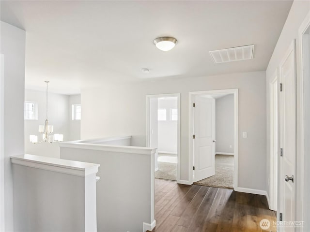 corridor featuring visible vents, an upstairs landing, dark wood-type flooring, baseboards, and a chandelier