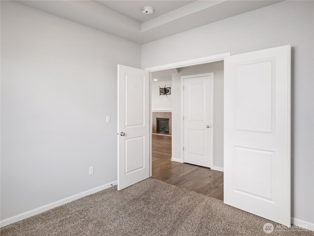 carpeted empty room with a tiled fireplace and baseboards