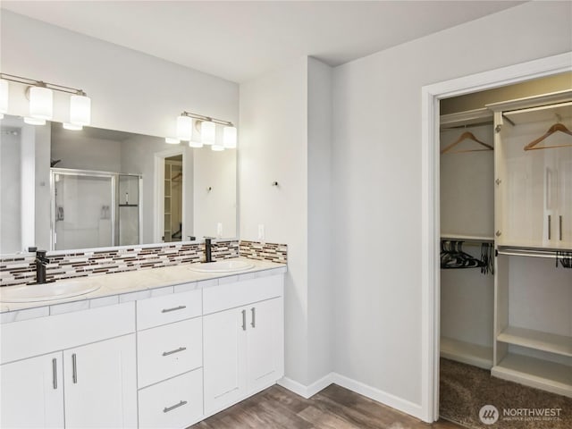 bathroom with a sink, decorative backsplash, a walk in closet, and a shower stall