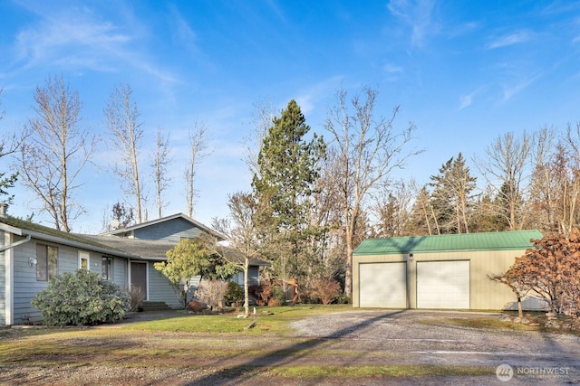 view of side of property featuring driveway, an attached garage, a lawn, and an outbuilding