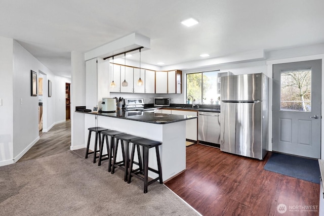 kitchen featuring dark countertops, a breakfast bar, a peninsula, stainless steel appliances, and white cabinetry