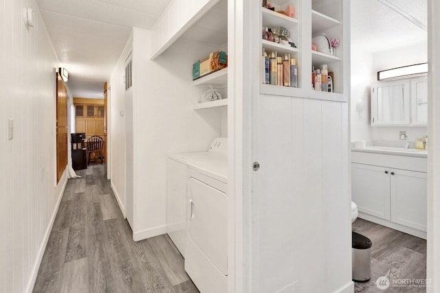 hallway with baseboards, a sink, light wood finished floors, and separate washer and dryer