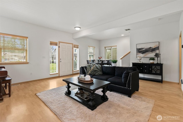 living room with light wood-type flooring, beam ceiling, visible vents, and baseboards