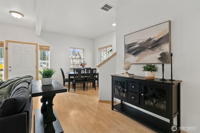 living room with beam ceiling, visible vents, baseboards, and wood finished floors