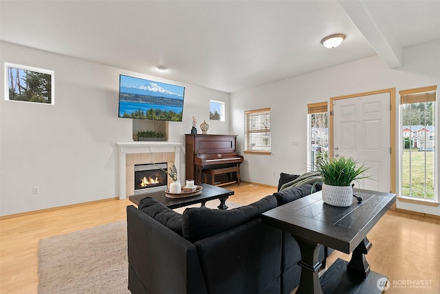 living area with beamed ceiling, a tile fireplace, light wood-style flooring, and baseboards