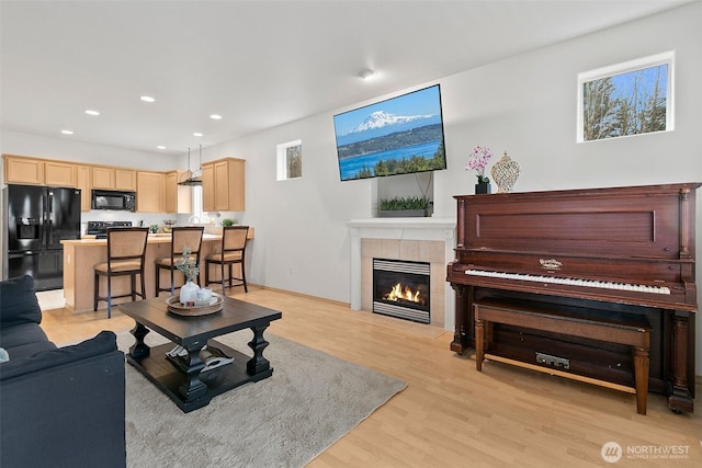 living area with light wood-style flooring, a tiled fireplace, and recessed lighting