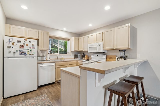 kitchen with a peninsula, white appliances, a breakfast bar, wood finished floors, and a sink