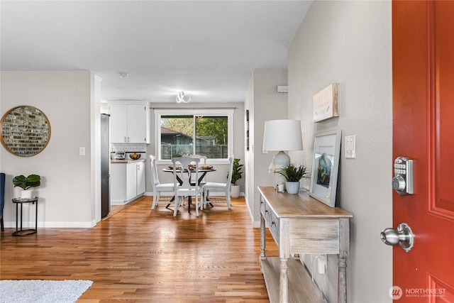 kitchen with tasteful backsplash, light wood-style flooring, freestanding refrigerator, white cabinetry, and baseboards