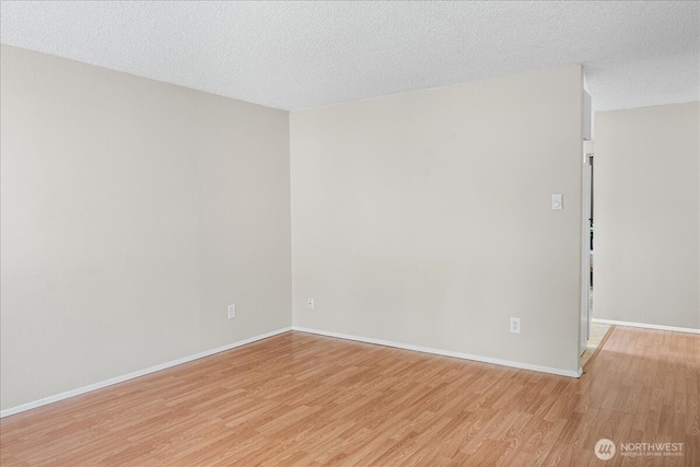 spare room with baseboards, light wood-style floors, and a textured ceiling