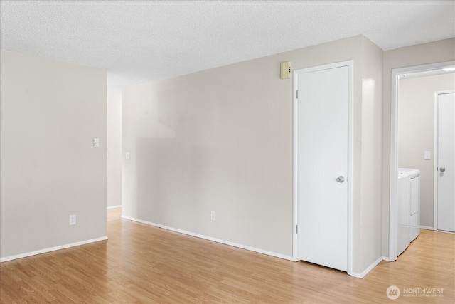 spare room featuring washer and dryer, light wood-style floors, baseboards, and a textured ceiling