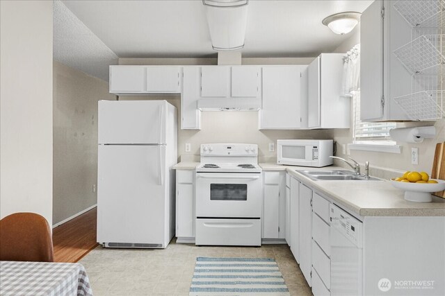 kitchen with light countertops, exhaust hood, white appliances, white cabinetry, and a sink