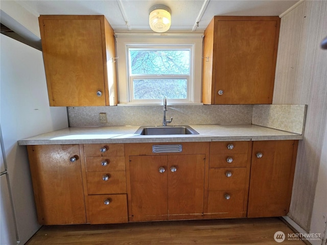 kitchen featuring light countertops, brown cabinetry, a sink, and decorative backsplash