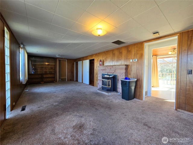 unfurnished living room with carpet floors, a wood stove, visible vents, and wooden walls