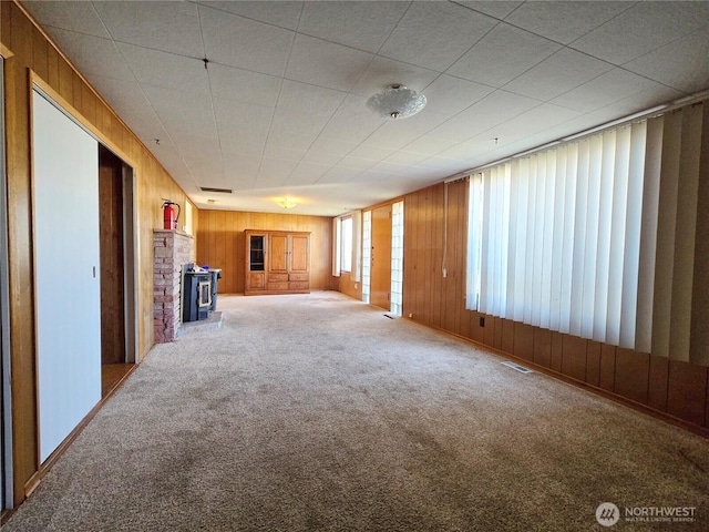 unfurnished living room featuring visible vents, wood walls, carpet, and a wood stove